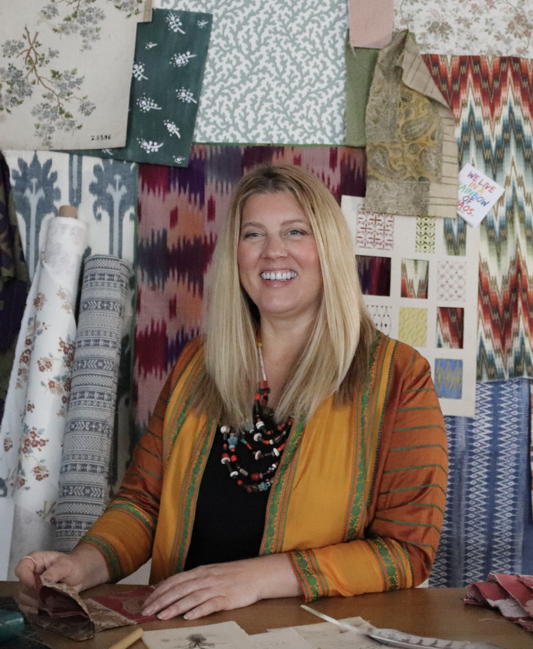 Kate Teyssier, a fabric and wallpaper designer, smiling in her studio among patterned textiles.