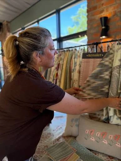 Kate Teyssier in profile, her hair in a ponytail, reaching out to a rail of her printed fabrics.