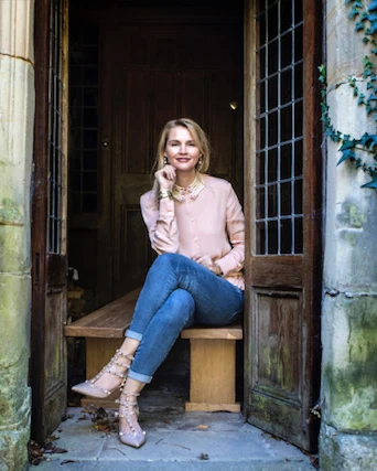 Keeley, an interior designer in Brisbane, sitting on a wooden bench in an old stone doorway framed by ivy.